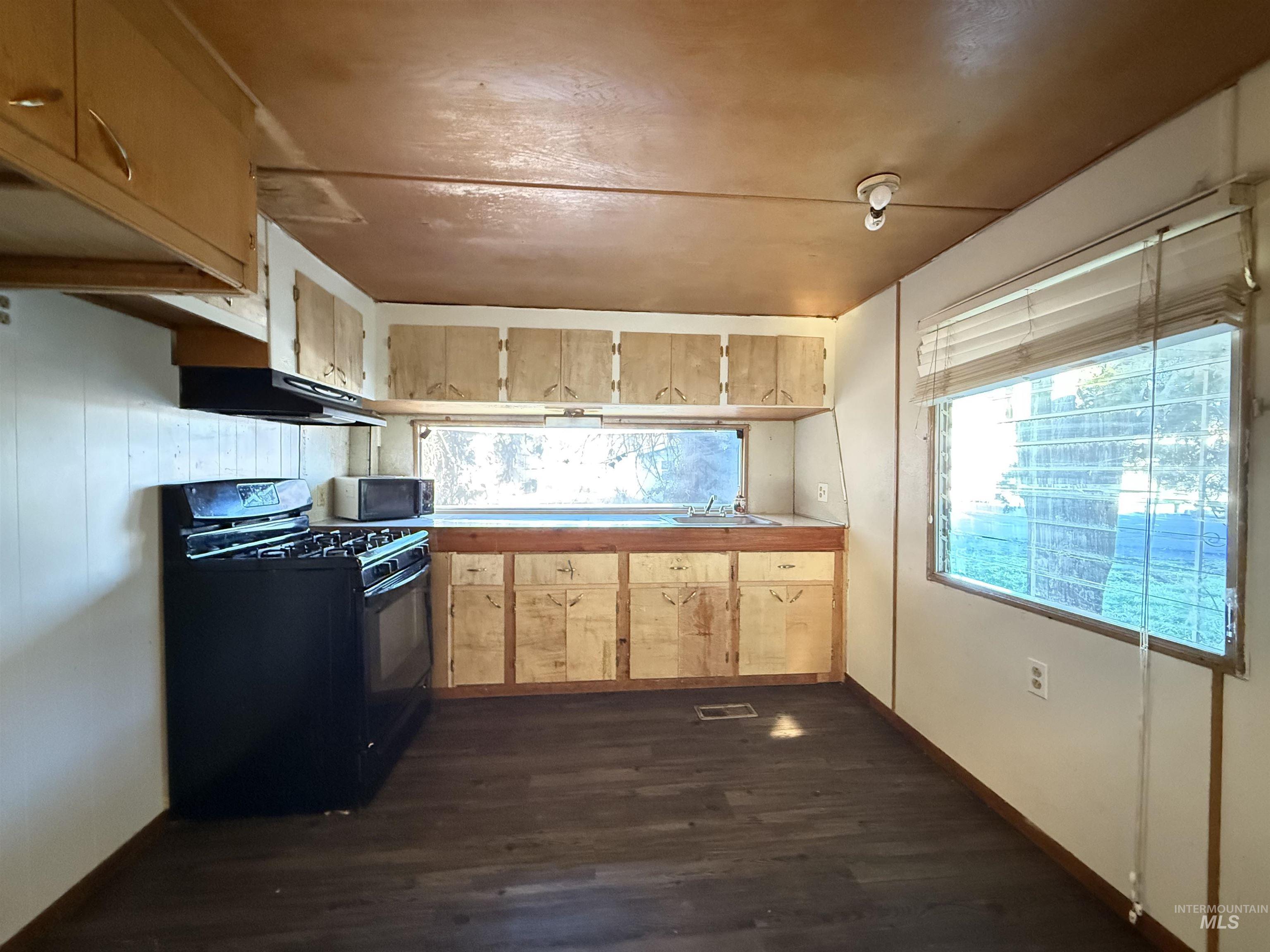 Kitchen with black appliances, dark wood-type flooring, light countertops, light brown cabinets, and under cabinet range hood