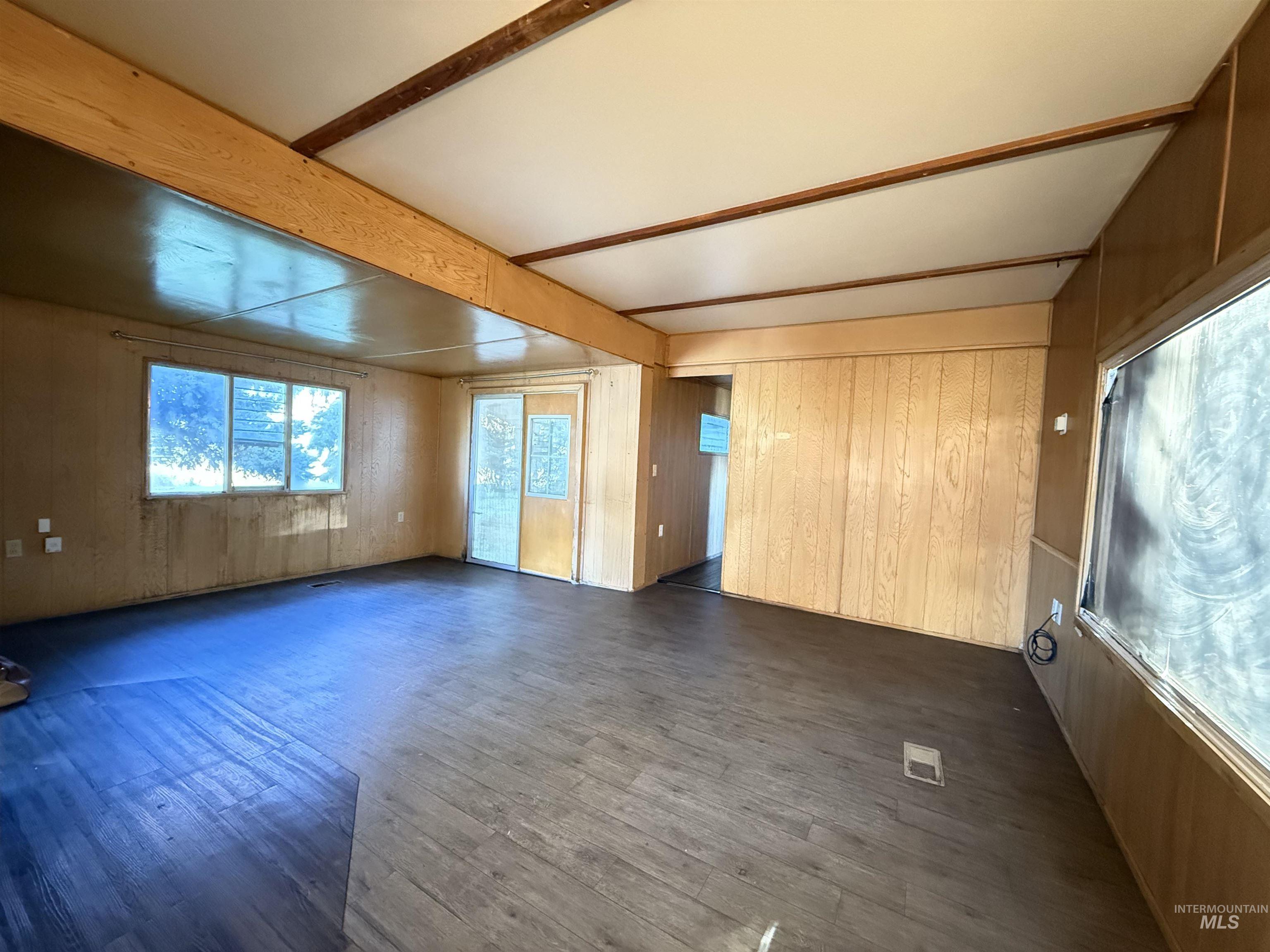 Spare room with wooden walls, beam ceiling, and dark wood-type flooring