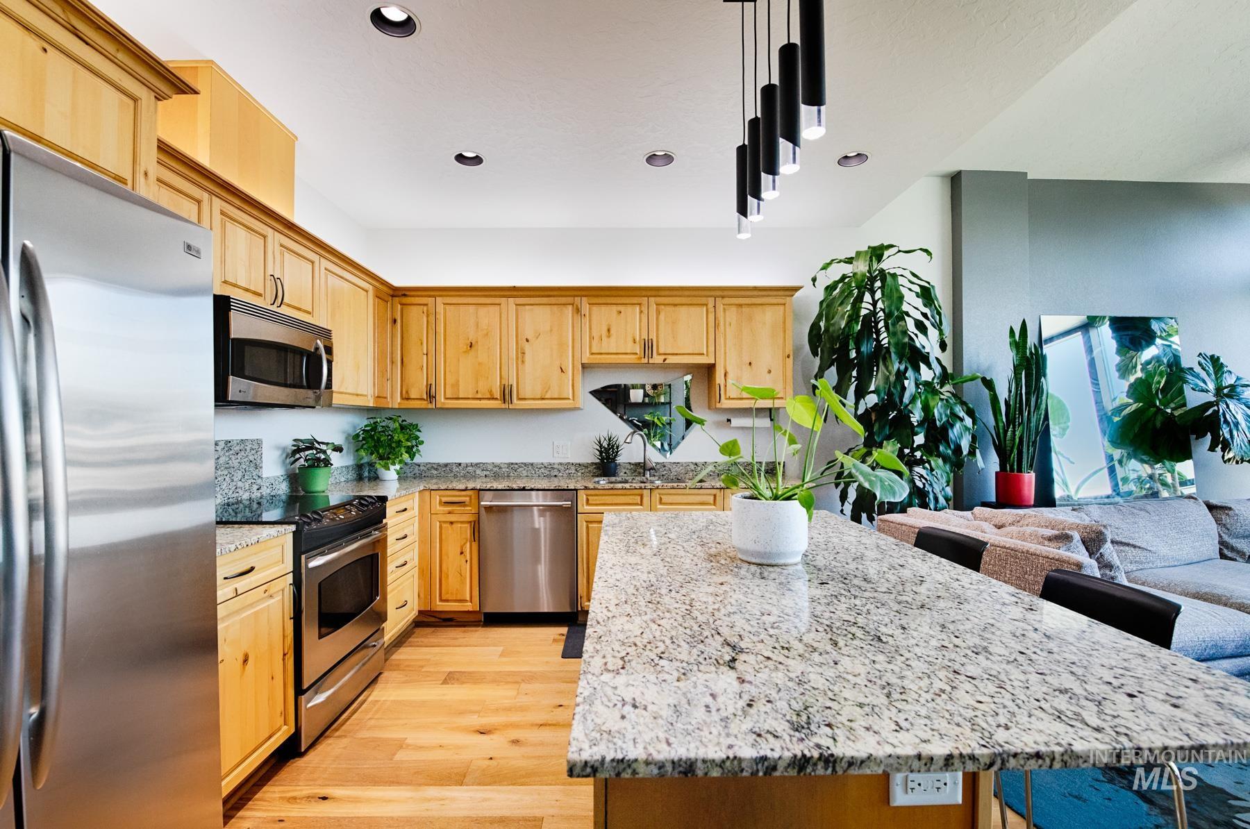 Kitchen featuring stainless steel appliances, light stone counters, light wood finished floors, a breakfast bar, and recessed lighting