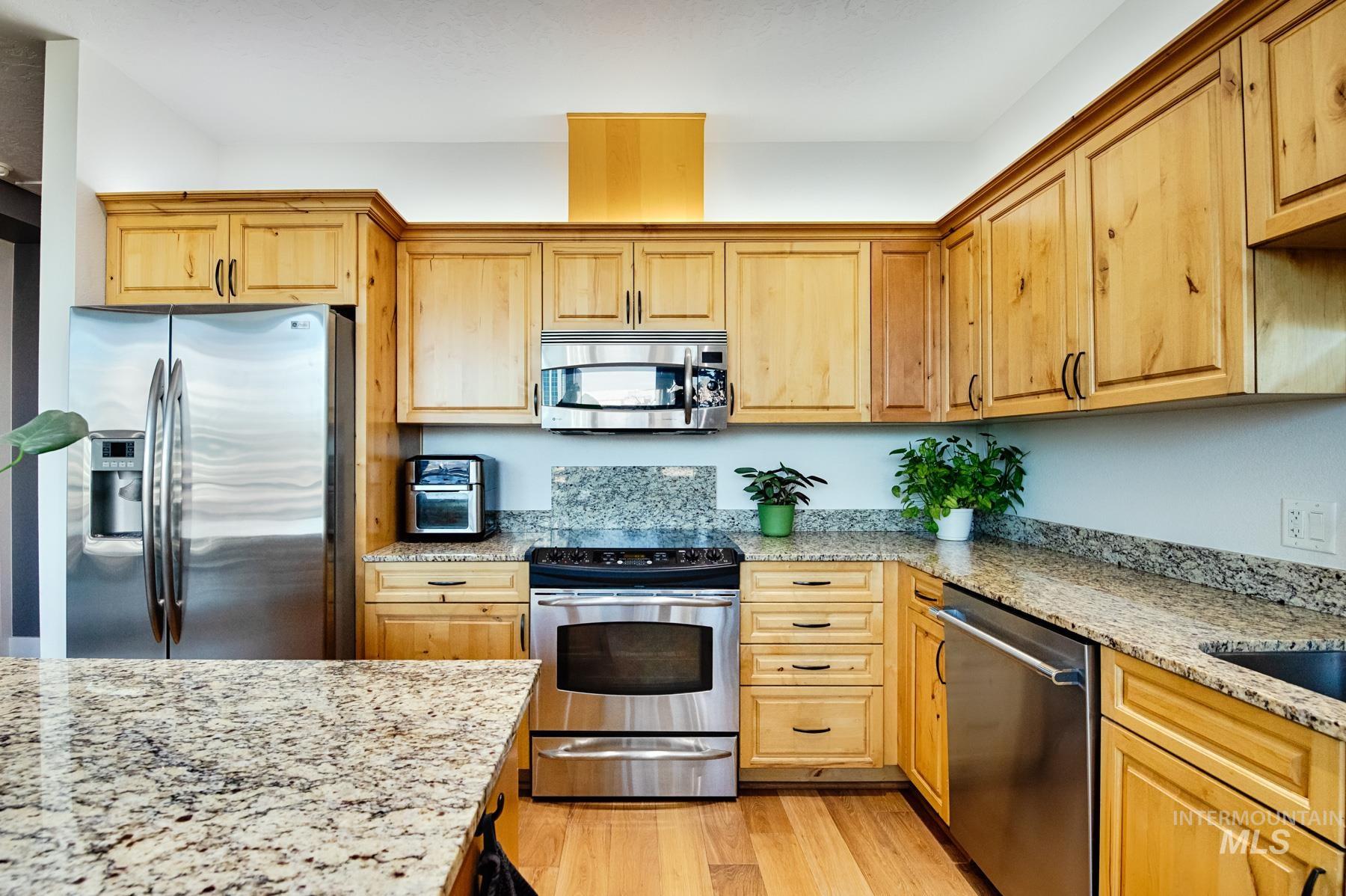 Kitchen with stainless steel appliances, light stone counters, light wood-style flooring, and light brown cabinets
