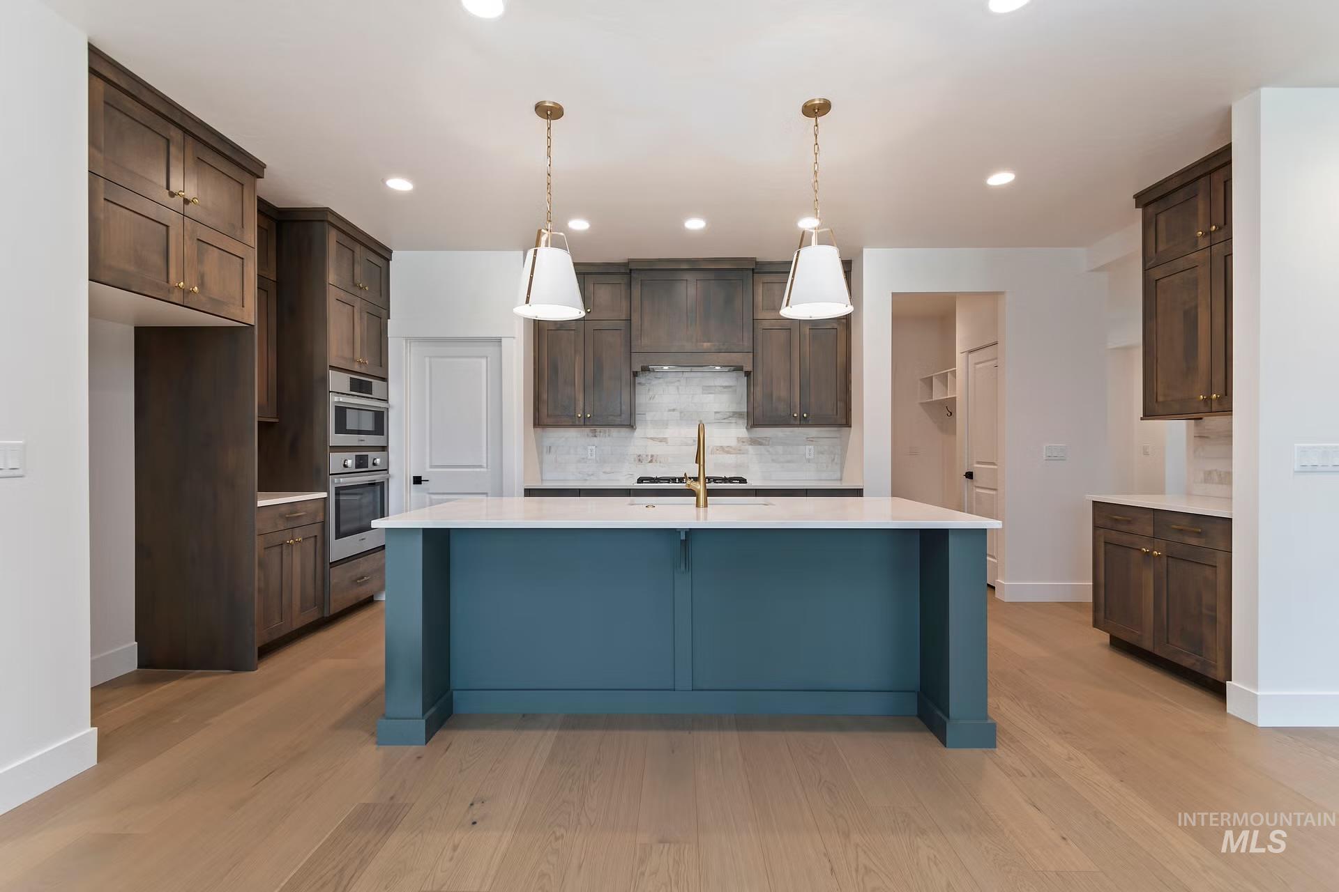 Kitchen with decorative backsplash, decorative light fixtures, a kitchen breakfast bar, light stone counters, and a center island with sink