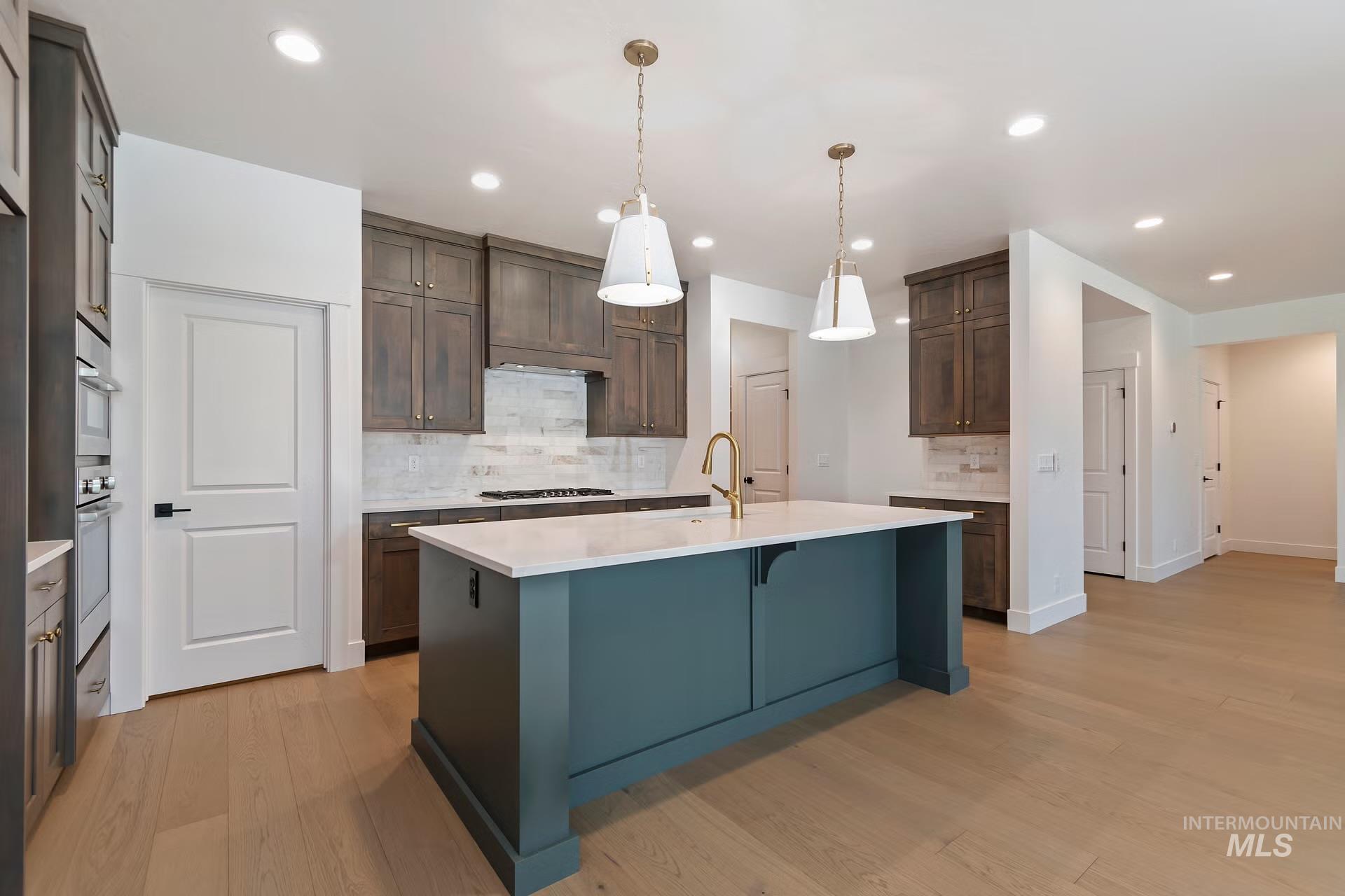 Kitchen featuring a kitchen bar, a kitchen island with sink, pendant lighting, light stone counters, and light wood finished floors