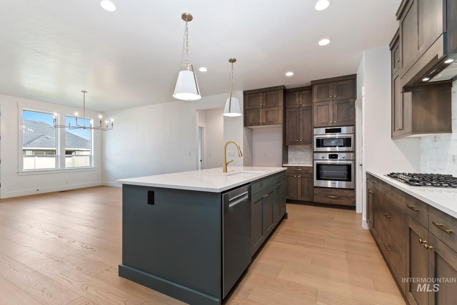 Kitchen with tasteful backsplash, pendant lighting, ventilation hood, a kitchen island with sink, and light wood-type flooring
