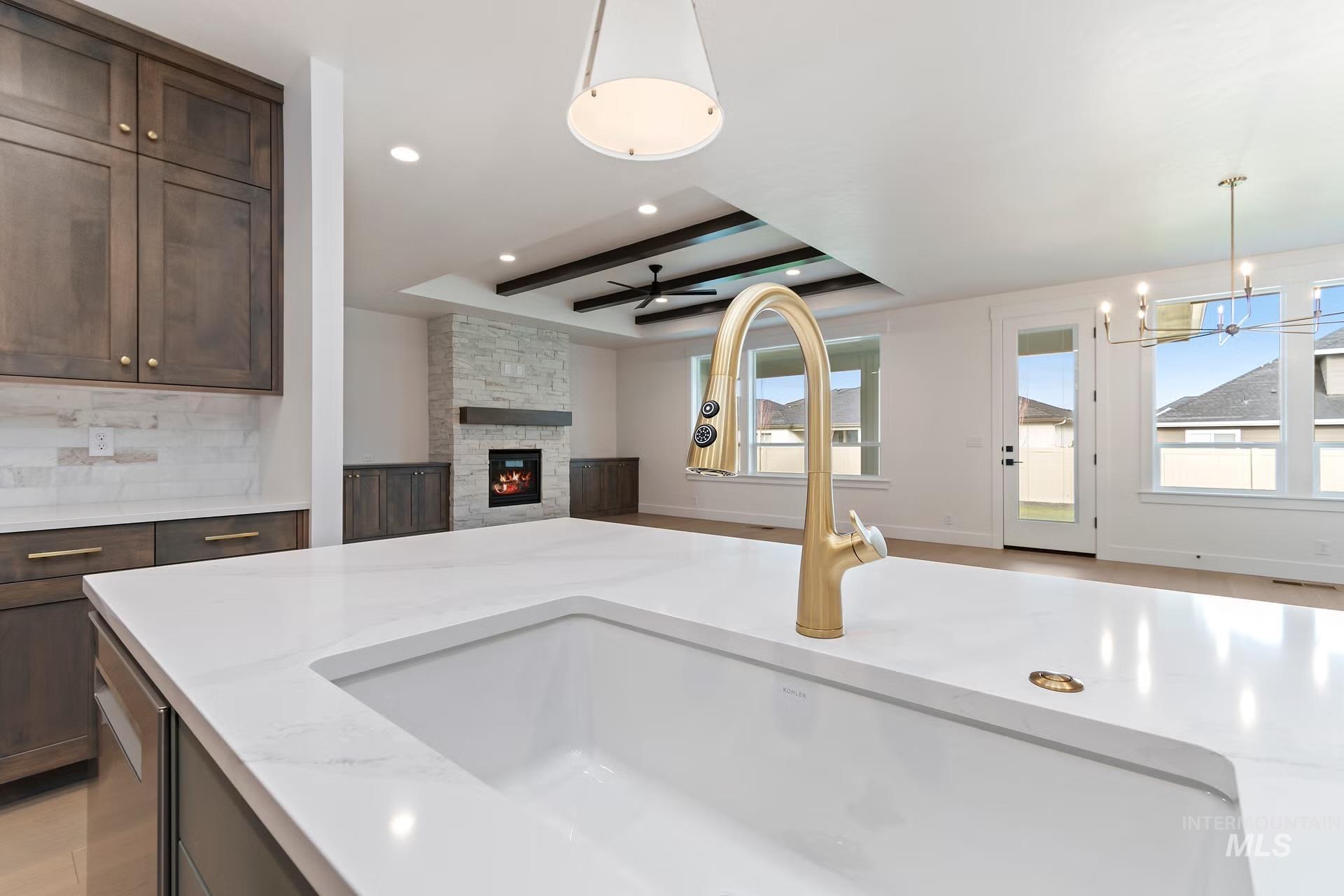 Kitchen with open floor plan, pendant lighting, light stone counters, a fireplace, and beam ceiling