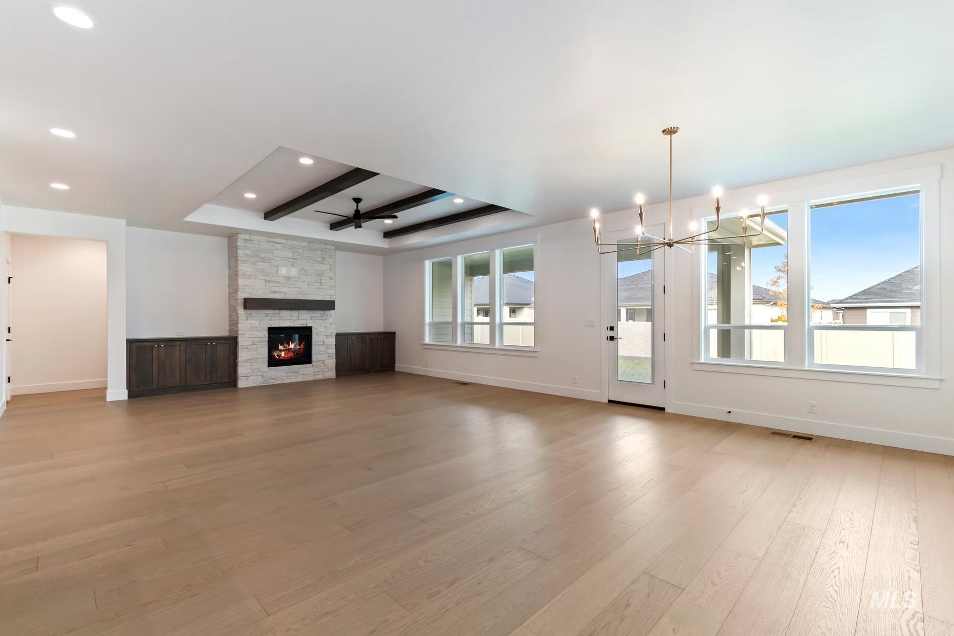 Unfurnished living room featuring a ceiling fan, light wood-style floors, a fireplace, a tray ceiling, and a chandelier