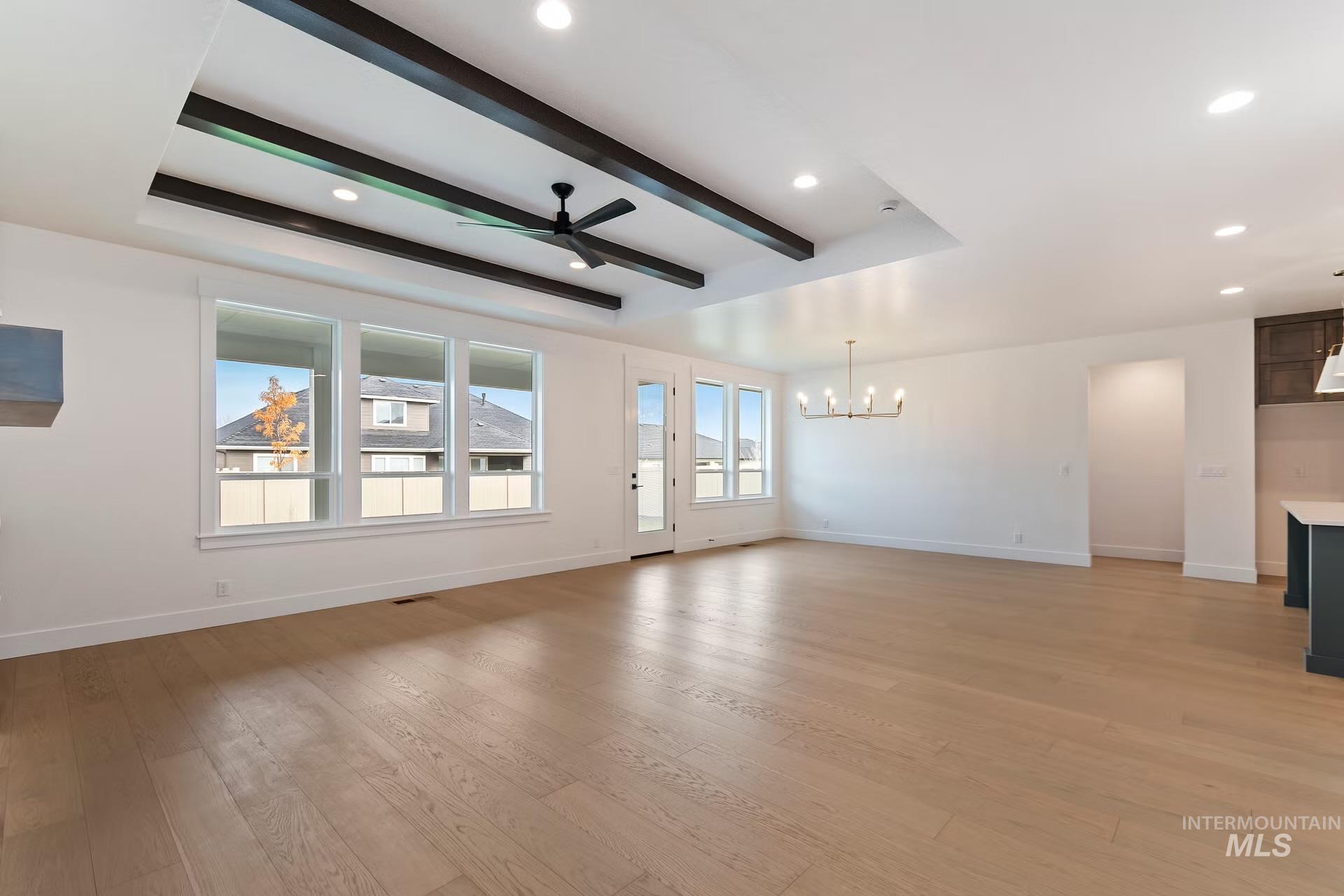 Unfurnished living room with a ceiling fan, beamed ceiling, light wood-type flooring, a chandelier, and recessed lighting