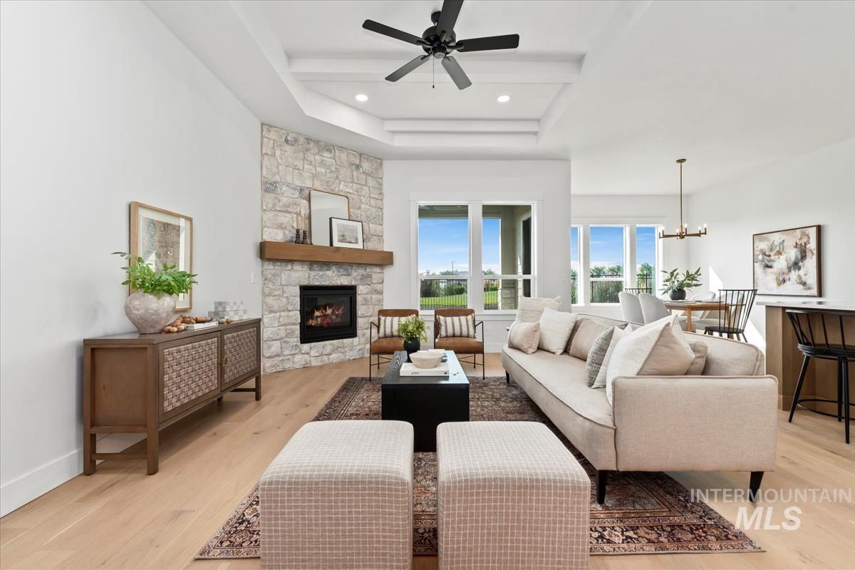 Living room with light wood-type flooring, a fireplace, a chandelier, a ceiling fan, and a tray ceiling
