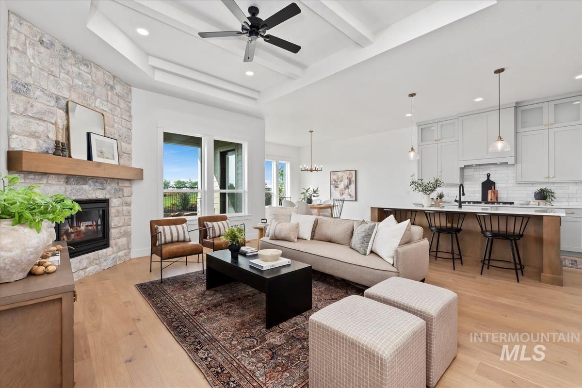 Living room with light wood-style flooring, beam ceiling, a chandelier, ceiling fan, and a stone fireplace