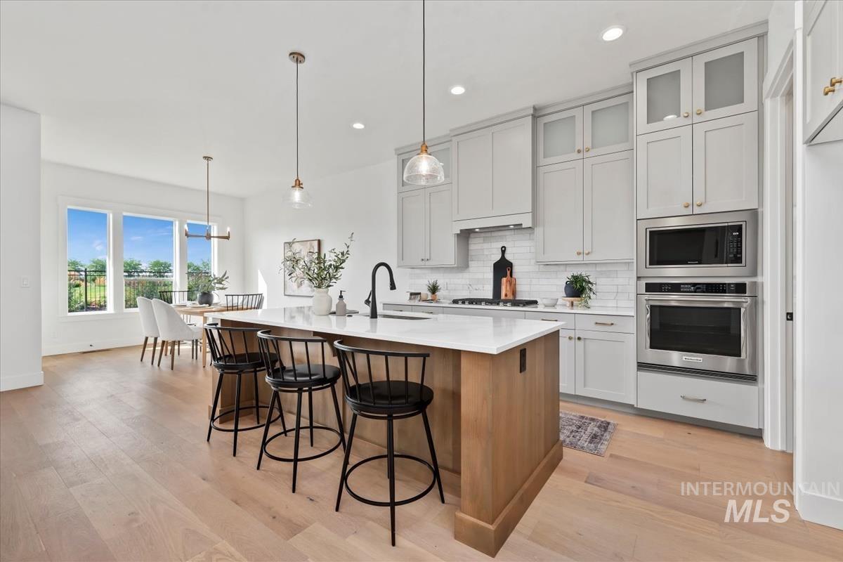 Kitchen with stainless steel appliances, hanging light fixtures, glass insert cabinets, brown cabinets, and recessed lighting