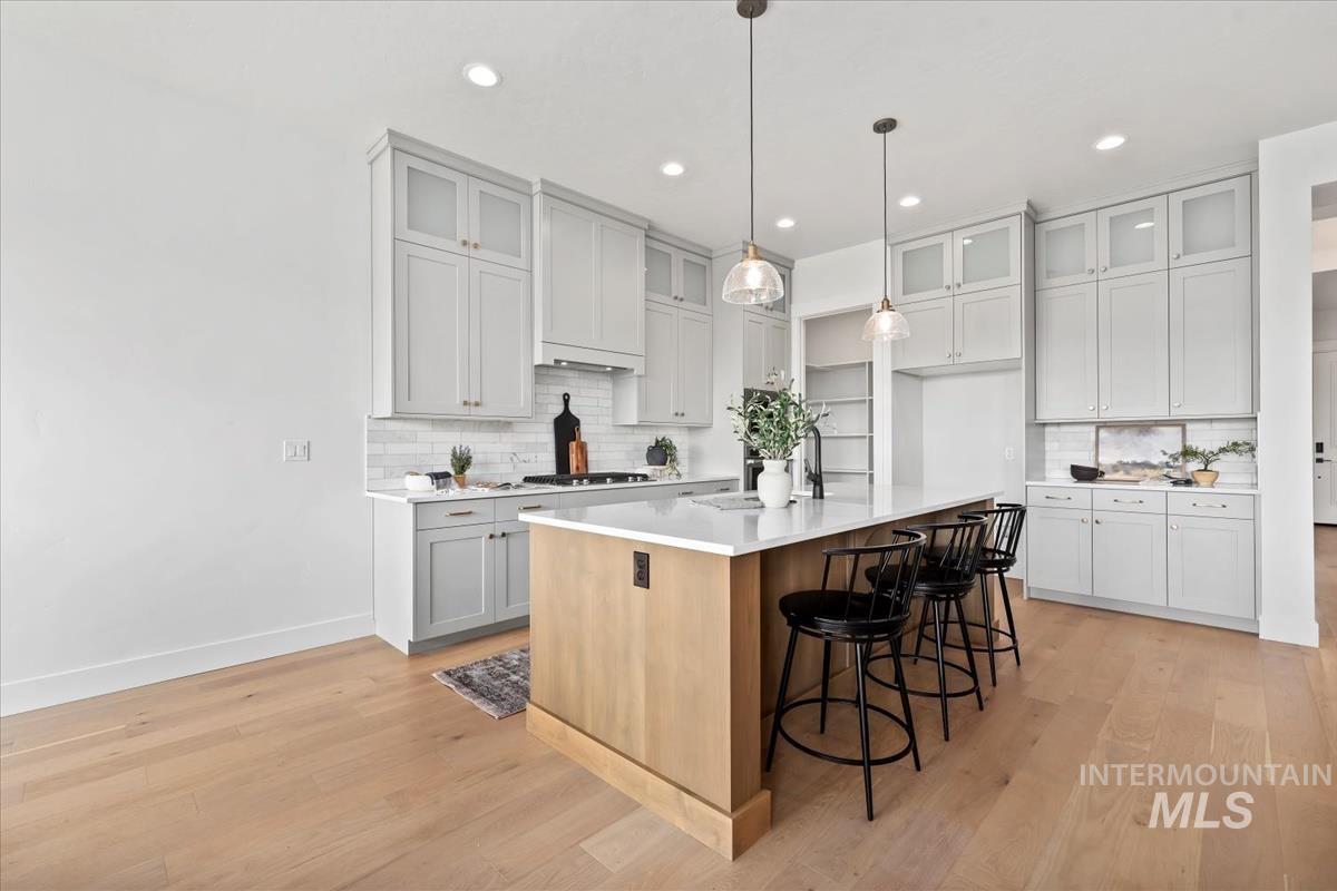 Kitchen with glass insert cabinets, a kitchen island with sink, a breakfast bar, light wood finished floors, and recessed lighting