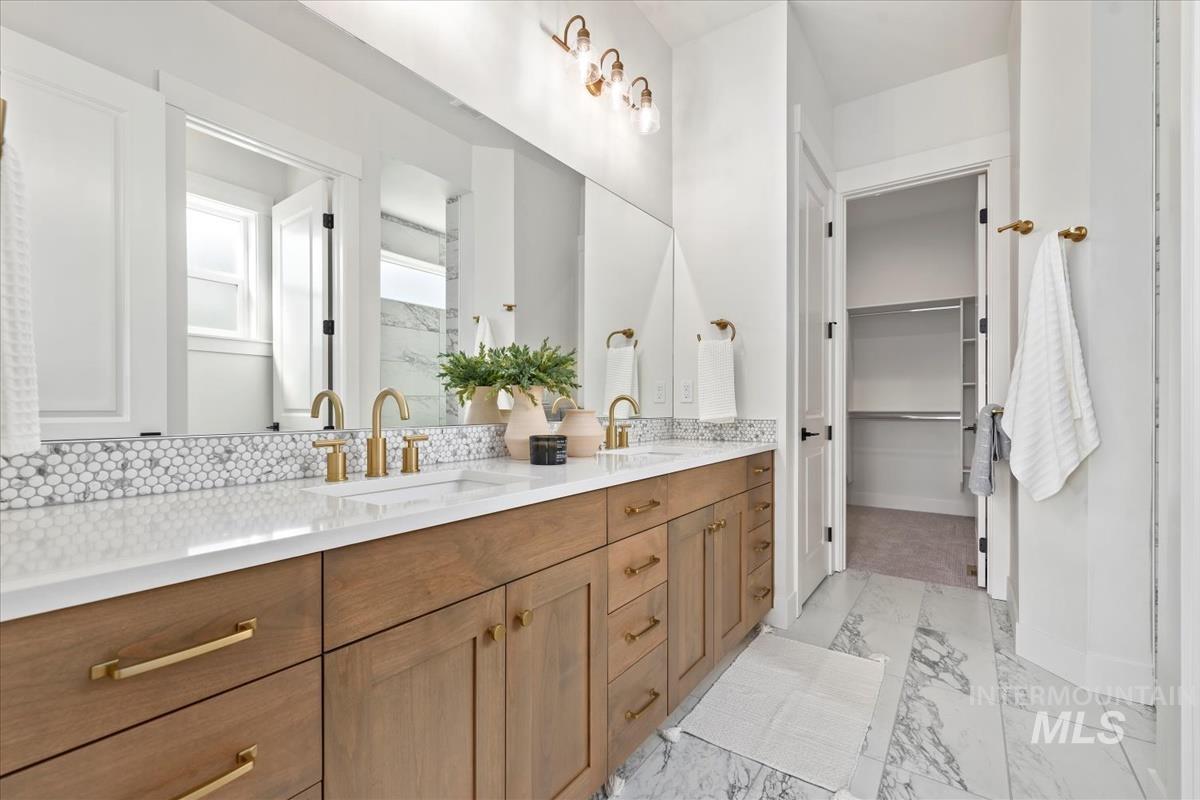 Bathroom featuring double vanity, light marble finish flooring, and a spacious closet
