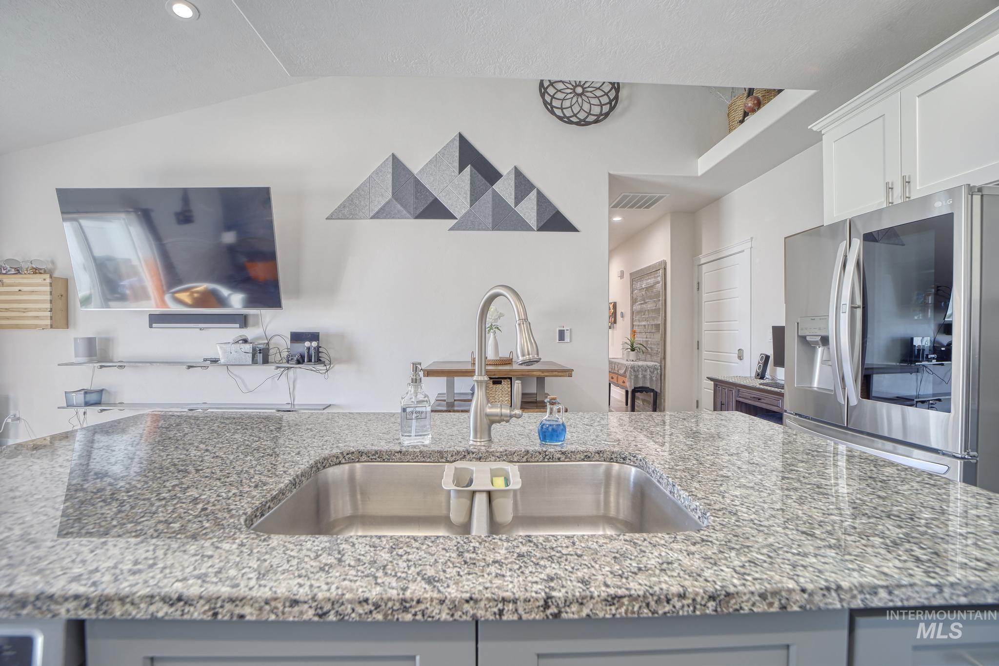 Kitchen with stainless steel fridge, light stone countertops, gray cabinets, recessed lighting, and an island with sink
