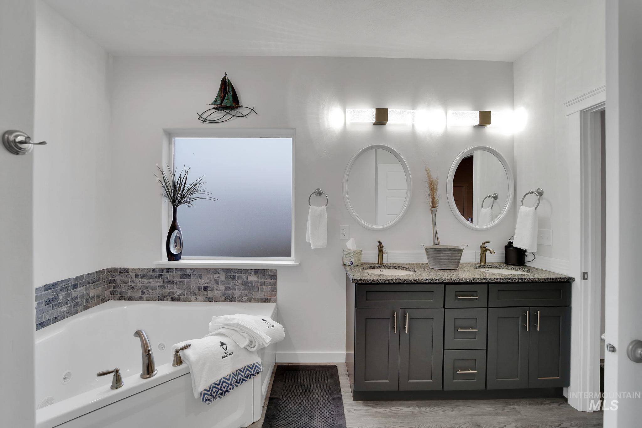 Bathroom featuring a tub with jets, double vanity, and light wood-type flooring