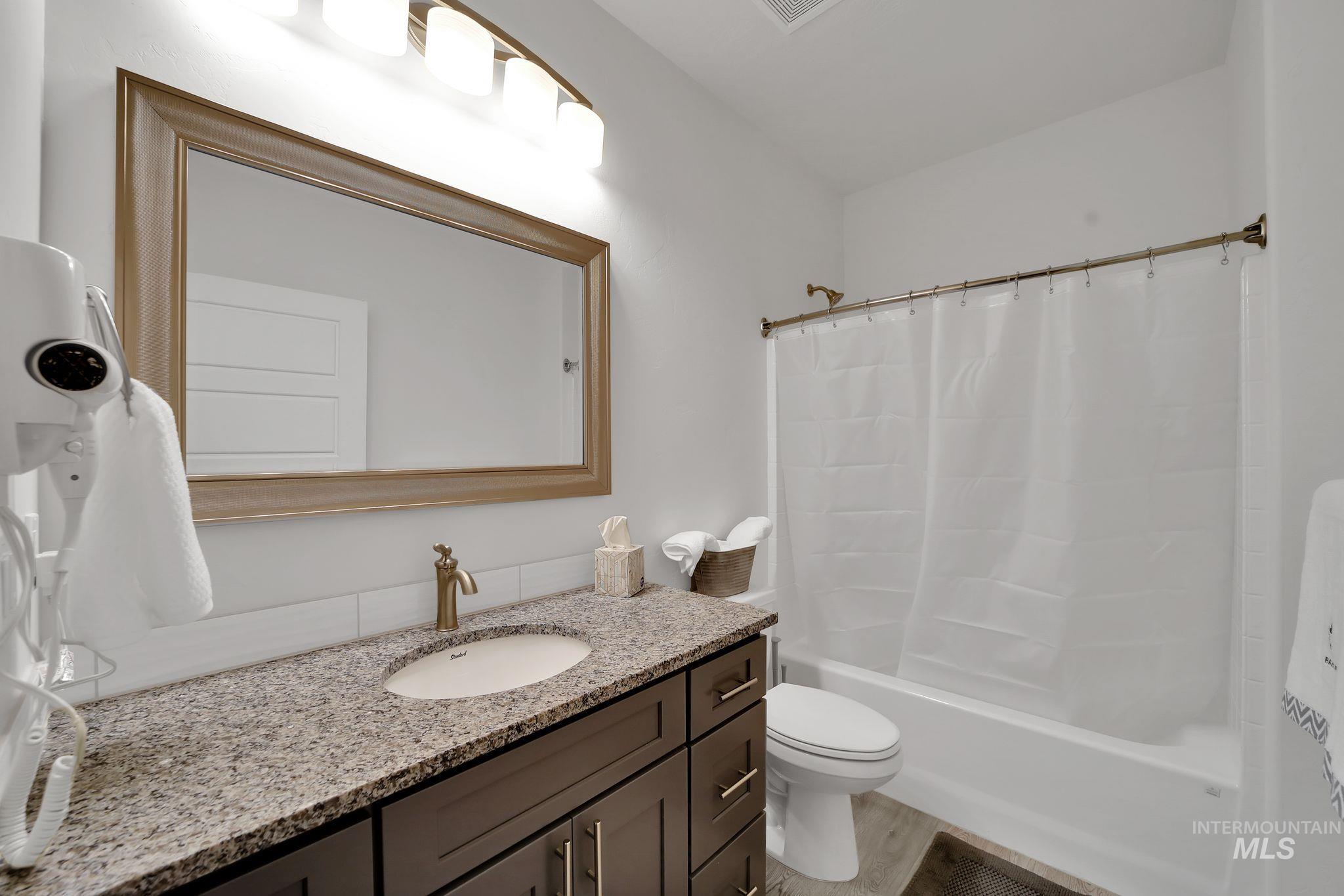 Full bathroom with vanity, shower / bath combo with shower curtain, and light wood-style flooring