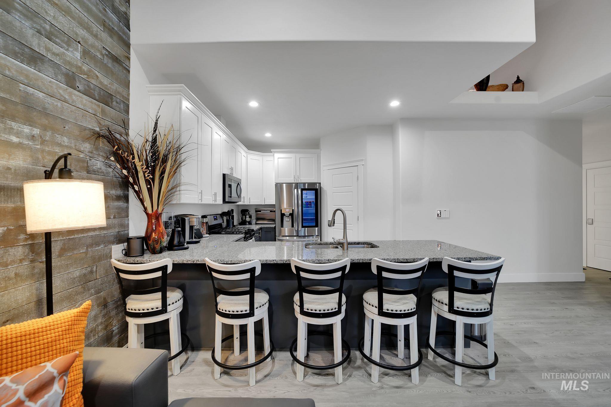Kitchen featuring a peninsula, a breakfast bar area, appliances with stainless steel finishes, white cabinetry, and light stone counters
