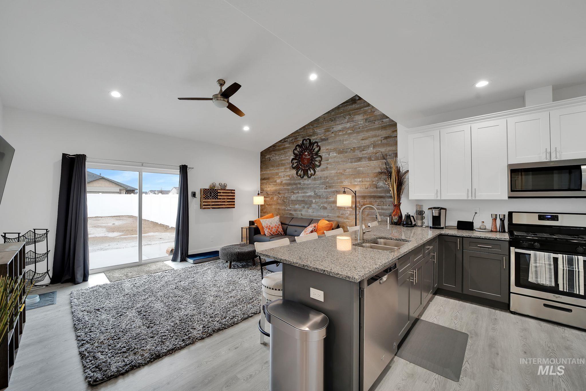 Kitchen with a peninsula, appliances with stainless steel finishes, light stone counters, white cabinets, and open floor plan