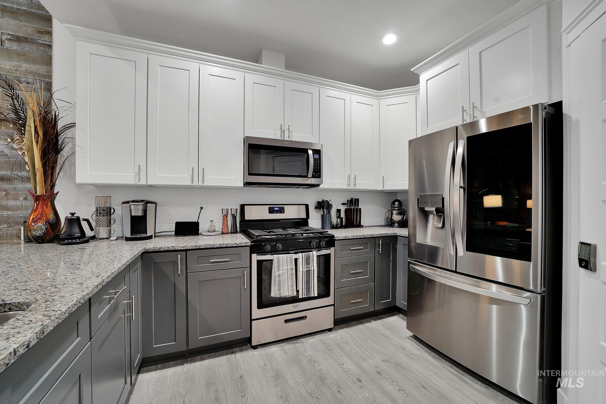 Kitchen featuring gray cabinets, appliances with stainless steel finishes, white cabinetry, and light stone counters