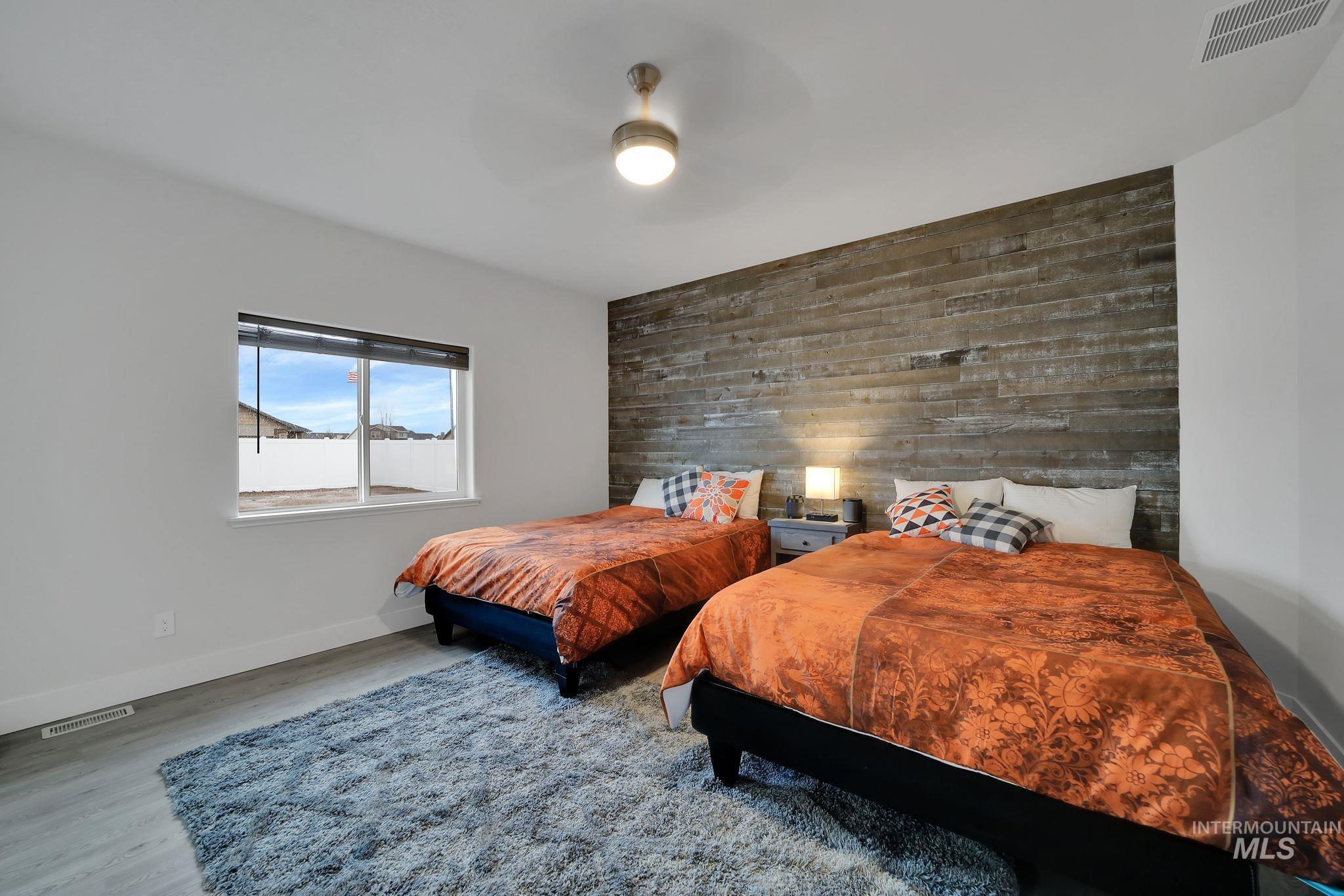 Bedroom with wooden walls, an accent wall, wood finished floors, and a ceiling fan