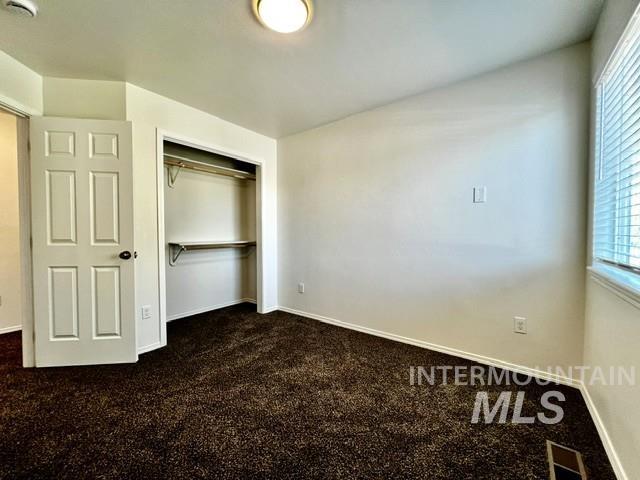Unfurnished bedroom featuring dark carpet, multiple windows, and a closet