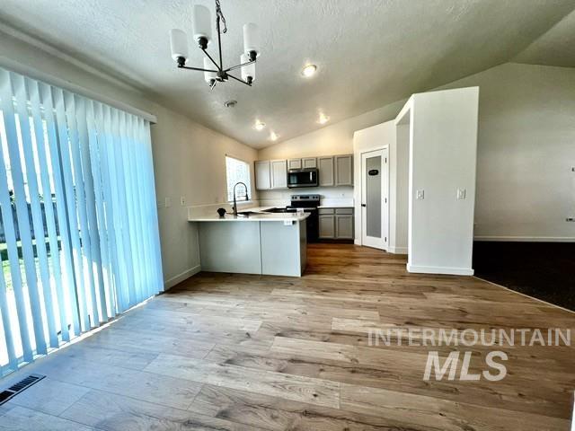 Kitchen featuring lofted ceiling, a chandelier, open floor plan, a peninsula, and wood finished floors
