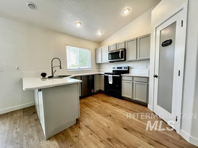 Kitchen featuring lofted ceiling, gray cabinetry, a peninsula, electric range oven, and stainless steel microwave