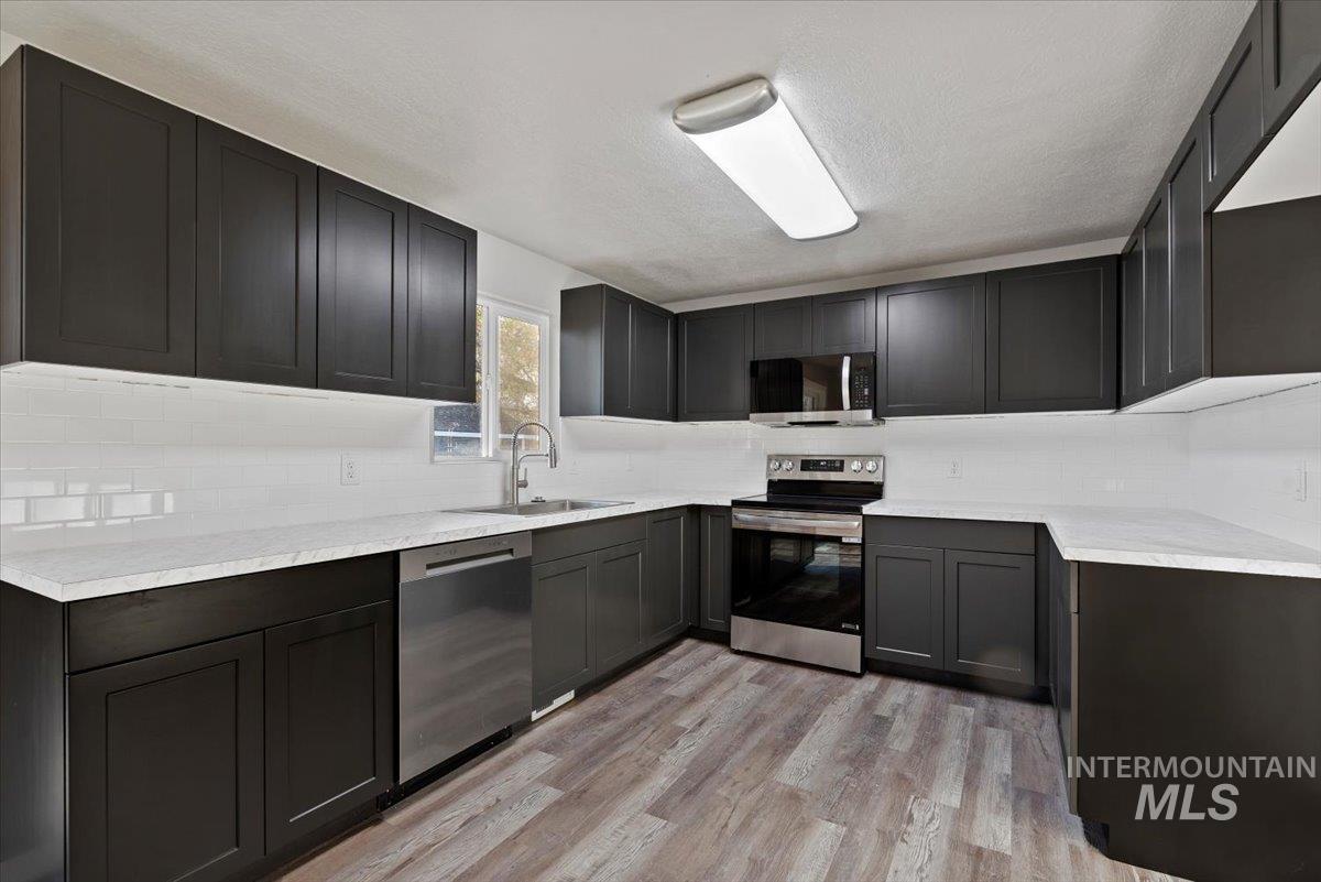 Kitchen with stainless steel appliances, backsplash, light wood-style floors, a textured ceiling, and dark cabinetry