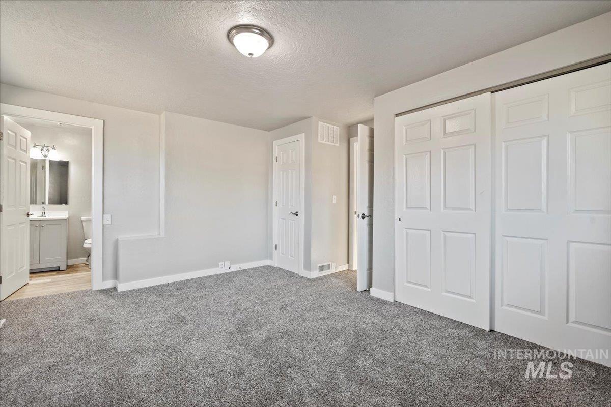 Unfurnished bedroom with a textured ceiling, carpet, a closet, and ensuite bathroom