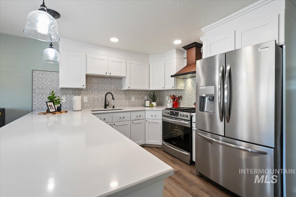 Kitchen with appliances with stainless steel finishes, white cabinetry, decorative light fixtures, wall chimney exhaust hood, and recessed lighting