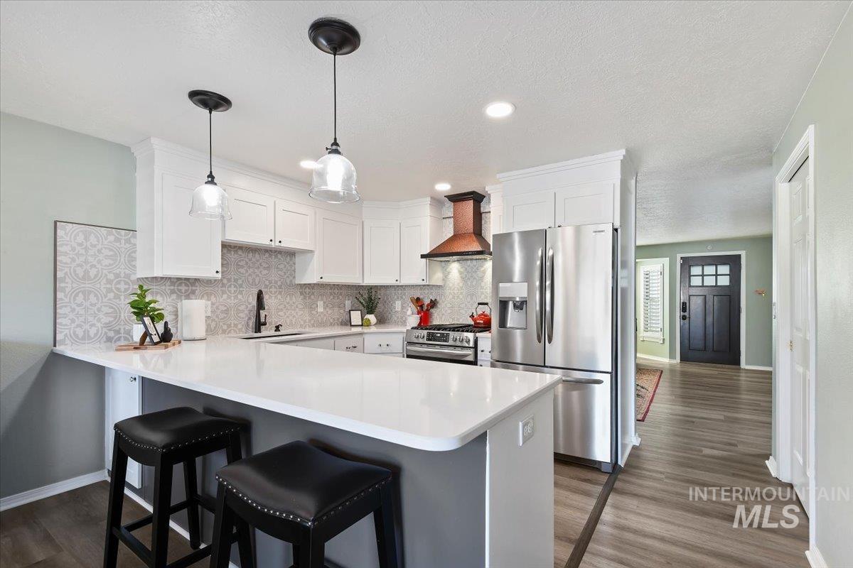 Kitchen with appliances with stainless steel finishes, white cabinets, custom exhaust hood, a peninsula, and hanging light fixtures