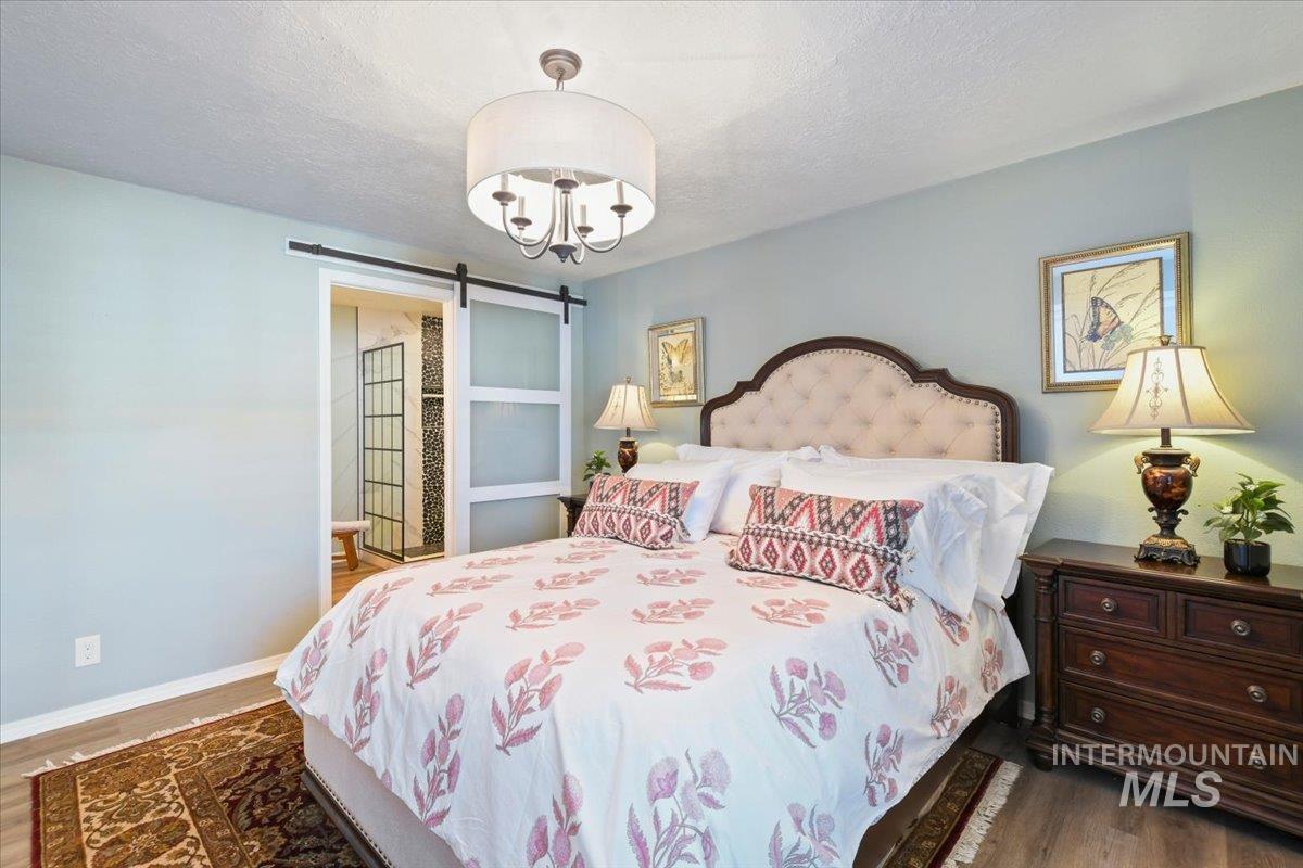Bedroom featuring a barn door, dark wood finished floors, a textured ceiling, and a chandelier