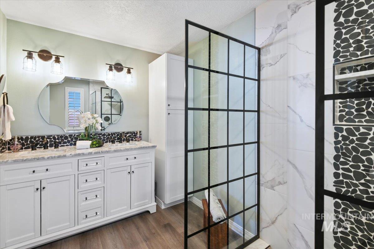 Bathroom with a marble finish shower, double vanity, dark wood-style flooring, and a textured ceiling