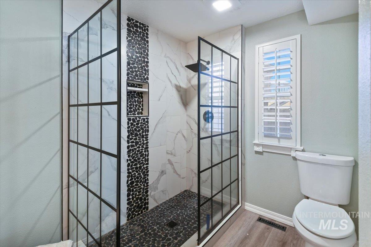 Full bath with a marble finish shower and wood finished floors