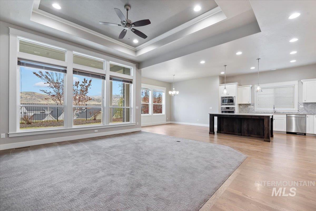 Unfurnished living room featuring a chandelier, recessed lighting, a raised ceiling, a ceiling fan, and light wood finished floors