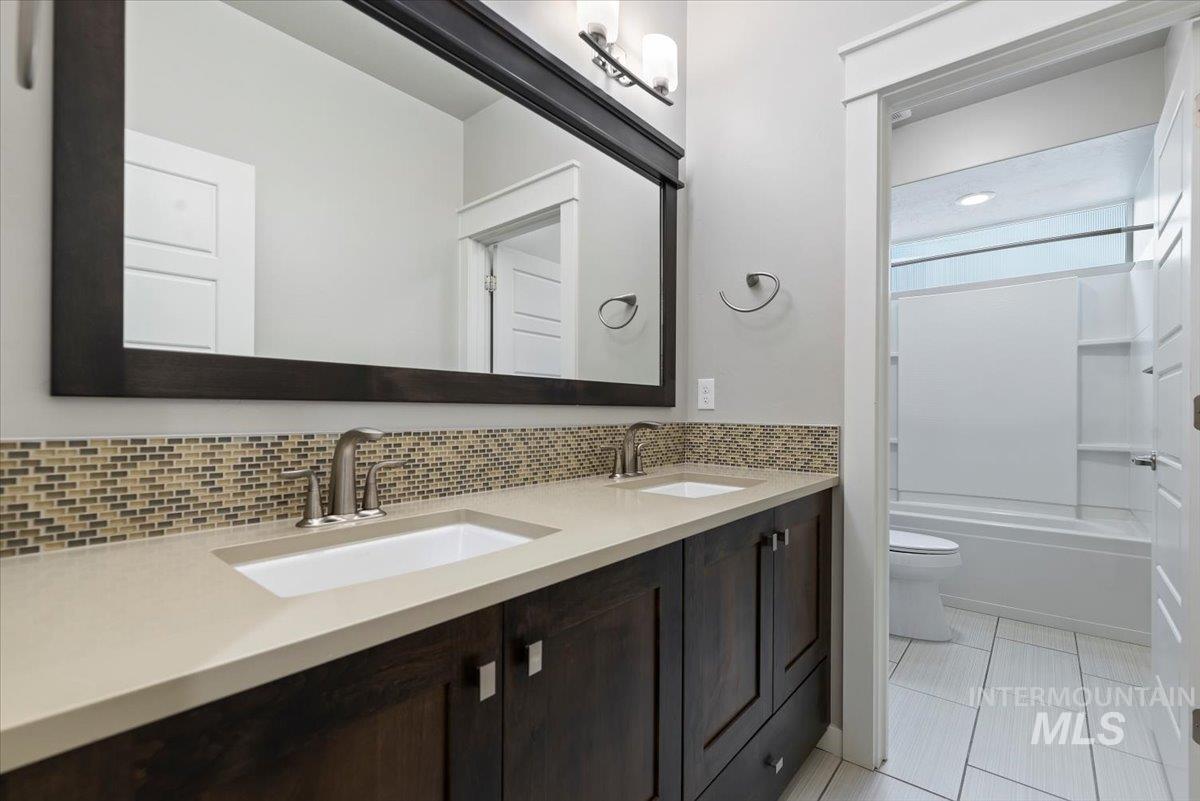 Bathroom with double vanity, shower / washtub combination, light tile patterned flooring, and decorative backsplash