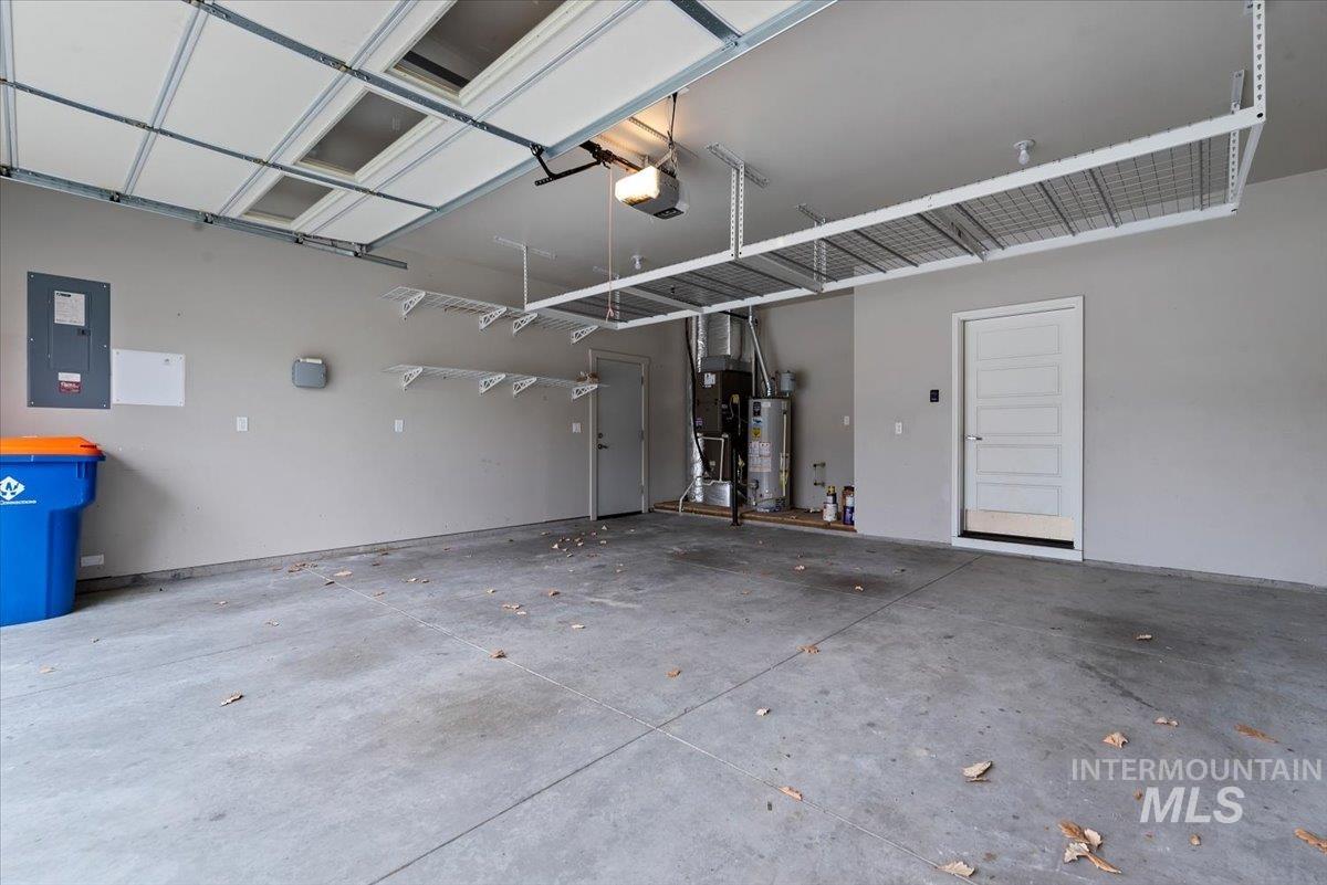 Garage featuring electric panel, gas water heater, a garage door opener, and heating unit
