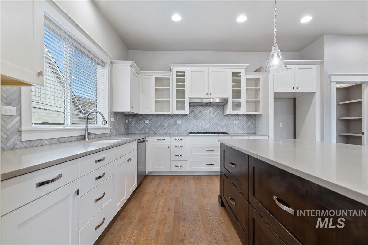 Kitchen with glass insert cabinets, white cabinetry, dark brown cabinetry, light wood-style flooring, and decorative light fixtures
