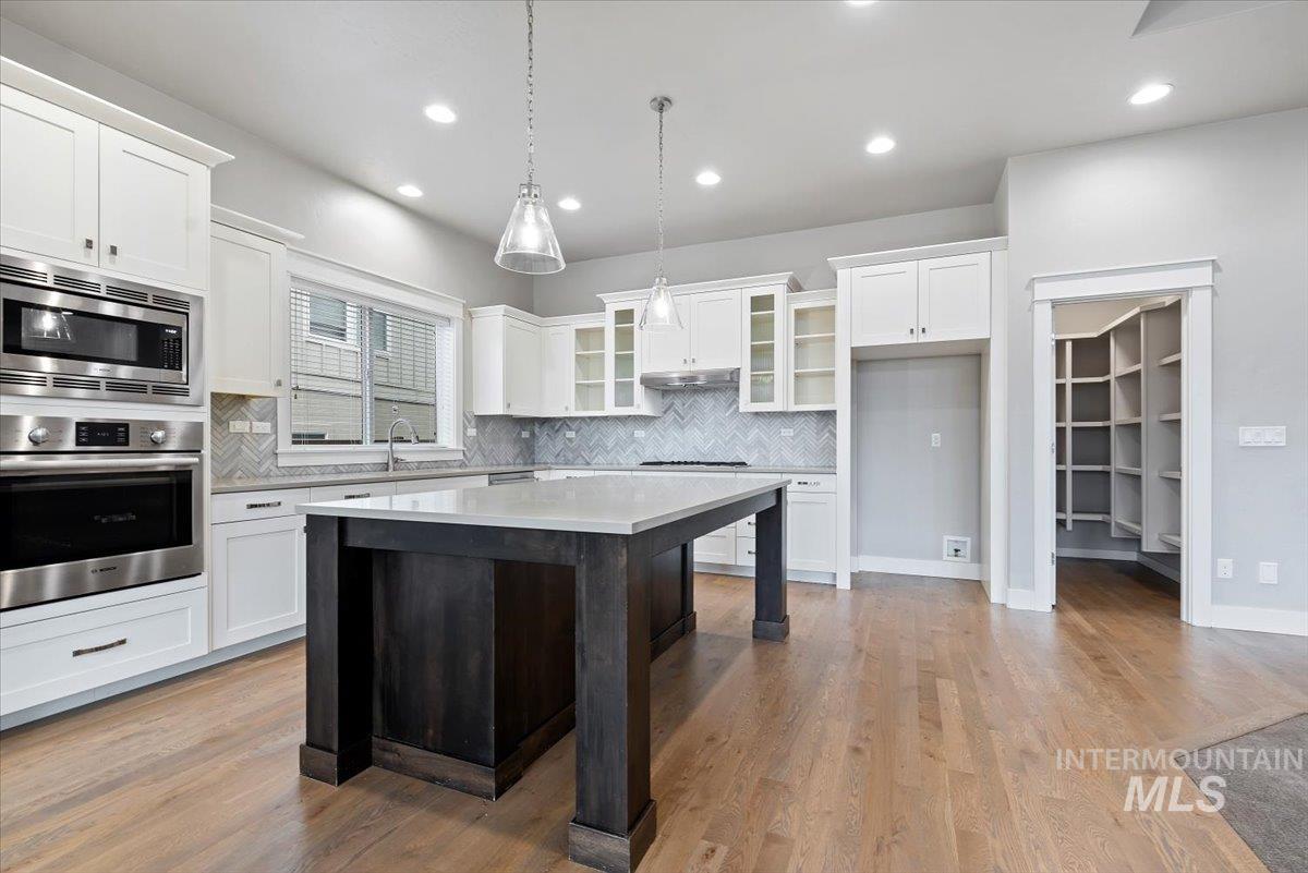 Kitchen with stainless steel appliances, glass insert cabinets, white cabinetry, a center island, and decorative backsplash