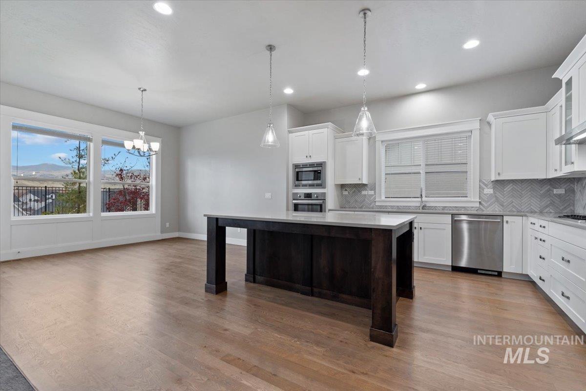 Kitchen with white cabinetry, pendant lighting, stainless steel appliances, dark wood finished floors, and tasteful backsplash