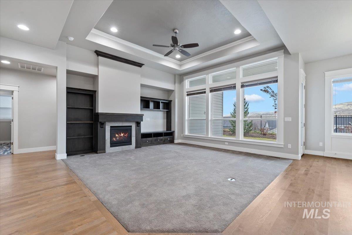 Unfurnished living room featuring light wood finished floors, a warm lit fireplace, ceiling fan, recessed lighting, and built in features