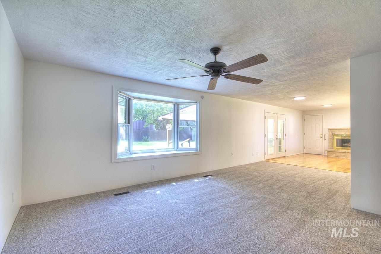Empty room featuring french doors, carpet floors, a fireplace, a textured ceiling, and a ceiling fan