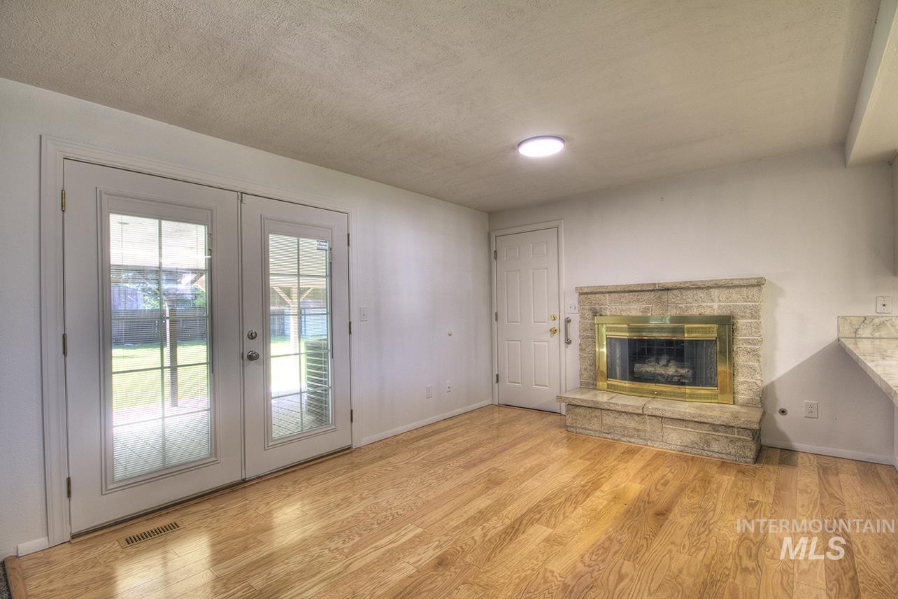 Unfurnished living room featuring french doors, a fireplace, light wood finished floors, and a textured ceiling