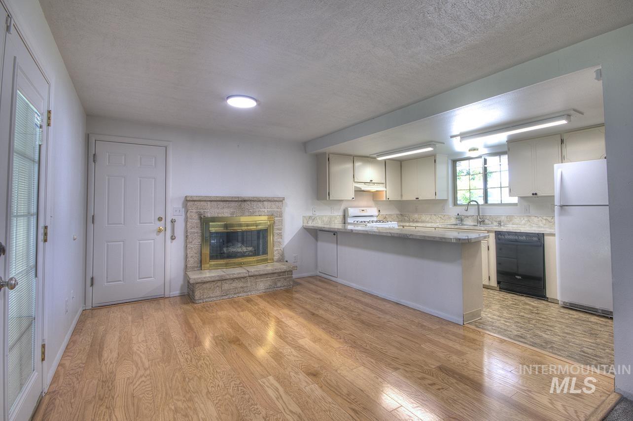 Kitchen featuring a peninsula, white appliances, light wood finished floors, a textured ceiling, and a stone fireplace