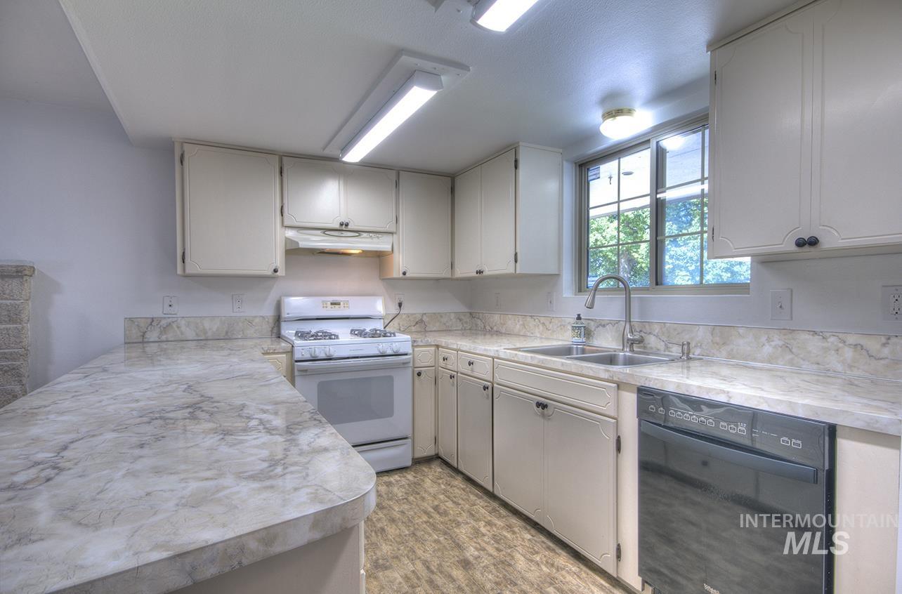 Kitchen featuring light countertops, dishwasher, white gas range, and a peninsula