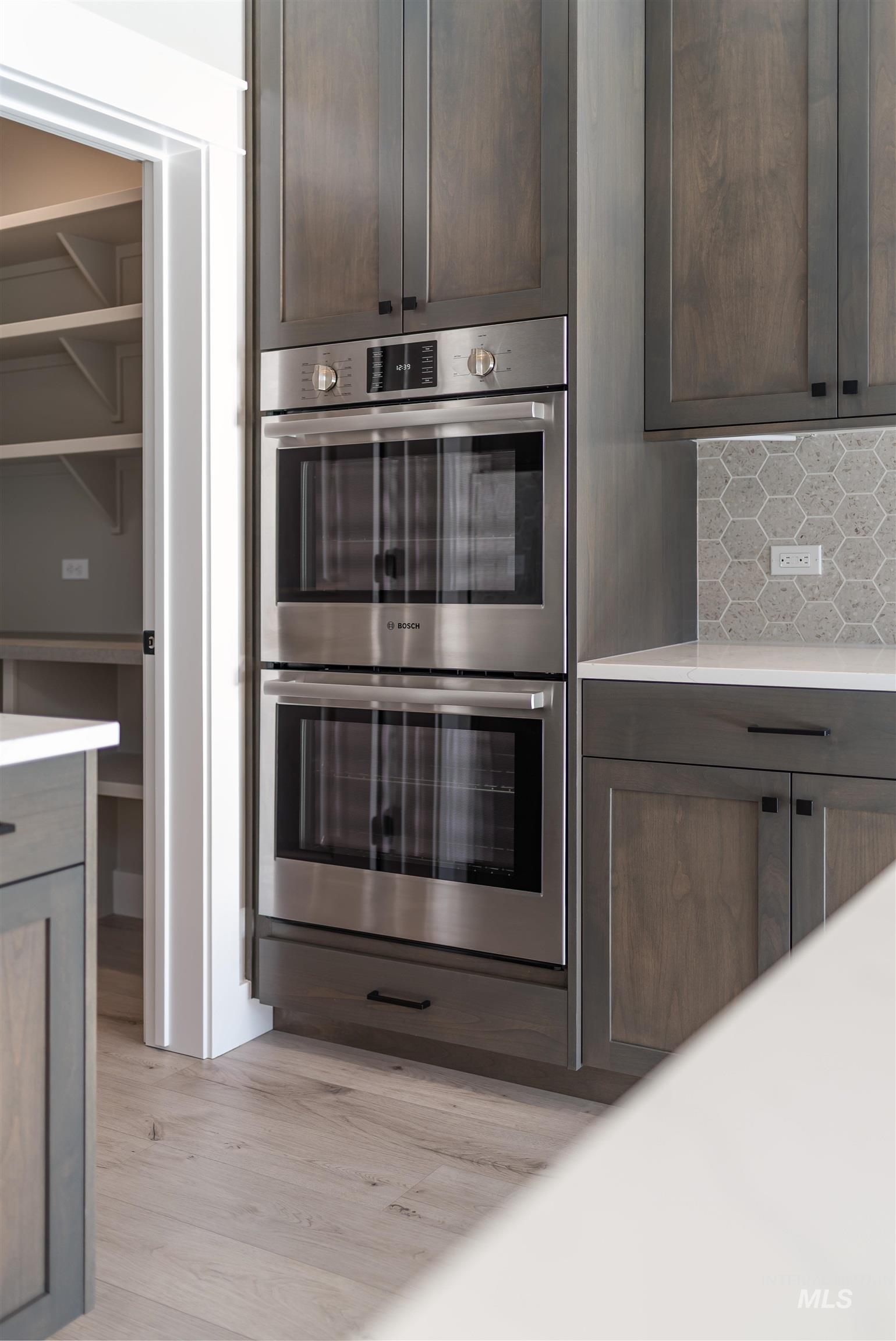 Kitchen featuring stainless steel double oven, dark brown cabinetry, backsplash, light wood-style floors, and light stone countertops