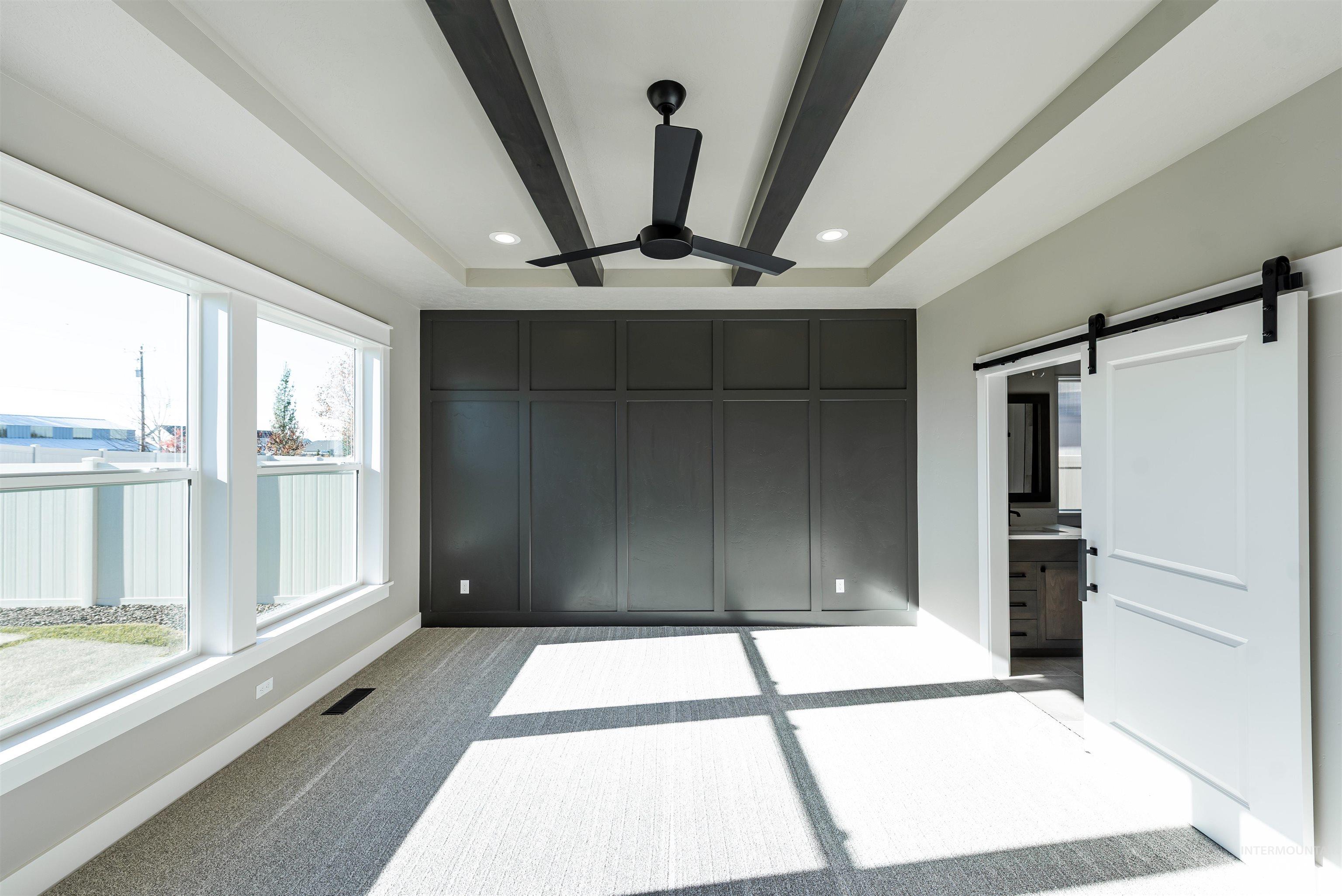 Unfurnished bedroom featuring a barn door, light colored carpet, ensuite bathroom, beam ceiling, and a ceiling fan