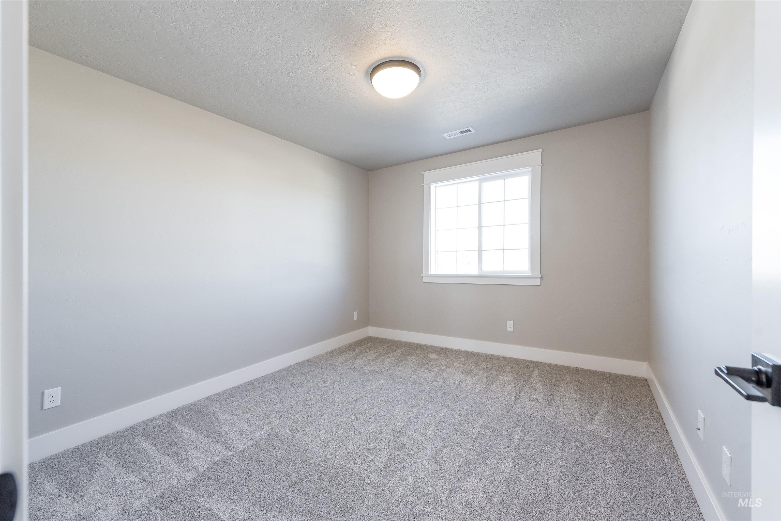 Carpeted spare room with a textured ceiling and baseboards
