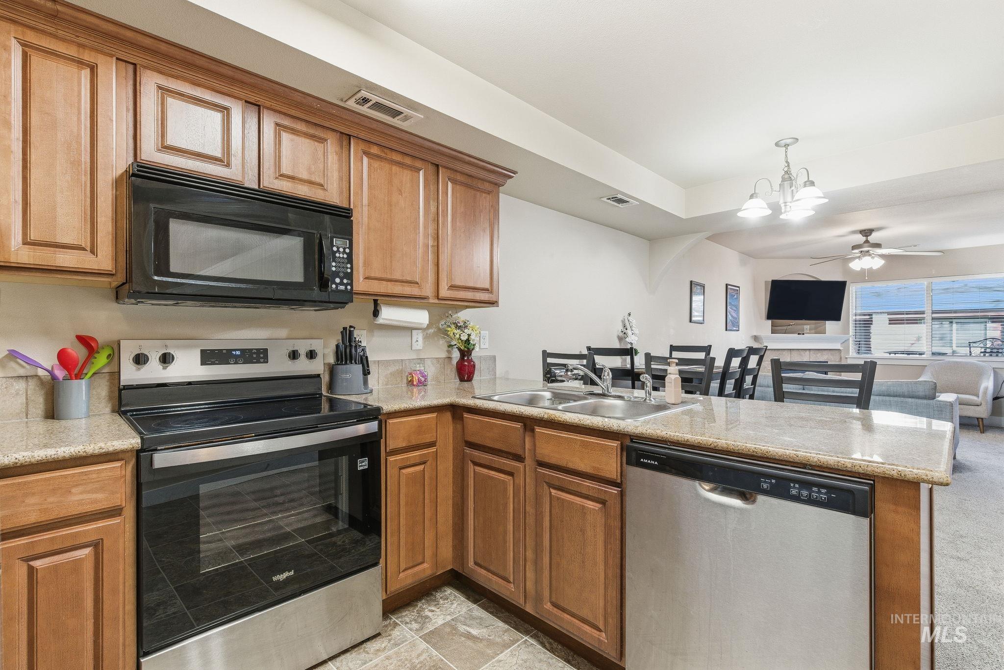 Kitchen featuring appliances with stainless steel finishes, brown cabinetry, a chandelier, pendant lighting, and open floor plan
