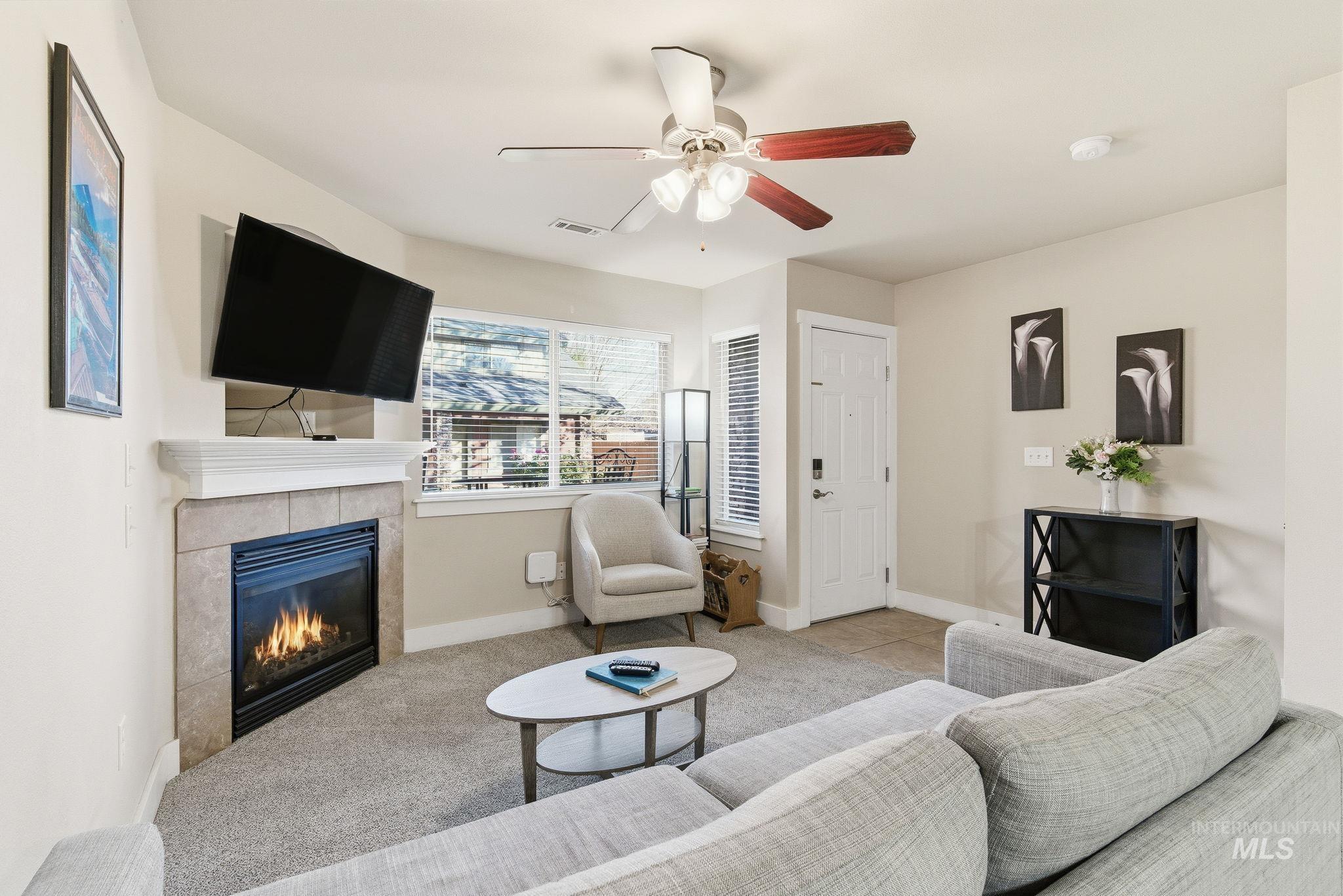 Carpeted living room with a tile fireplace and a ceiling fan