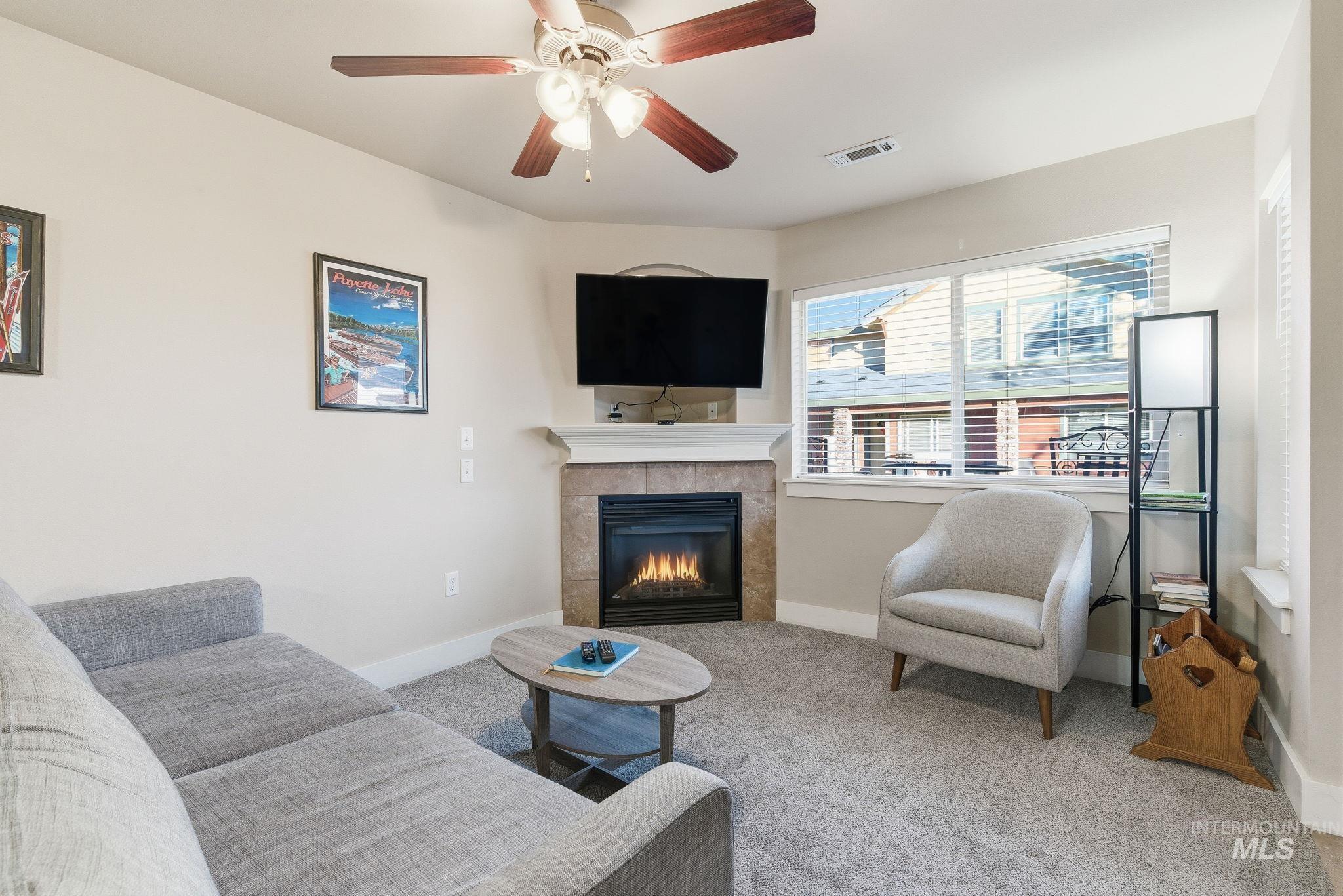 Living area featuring a fireplace, carpet, and ceiling fan