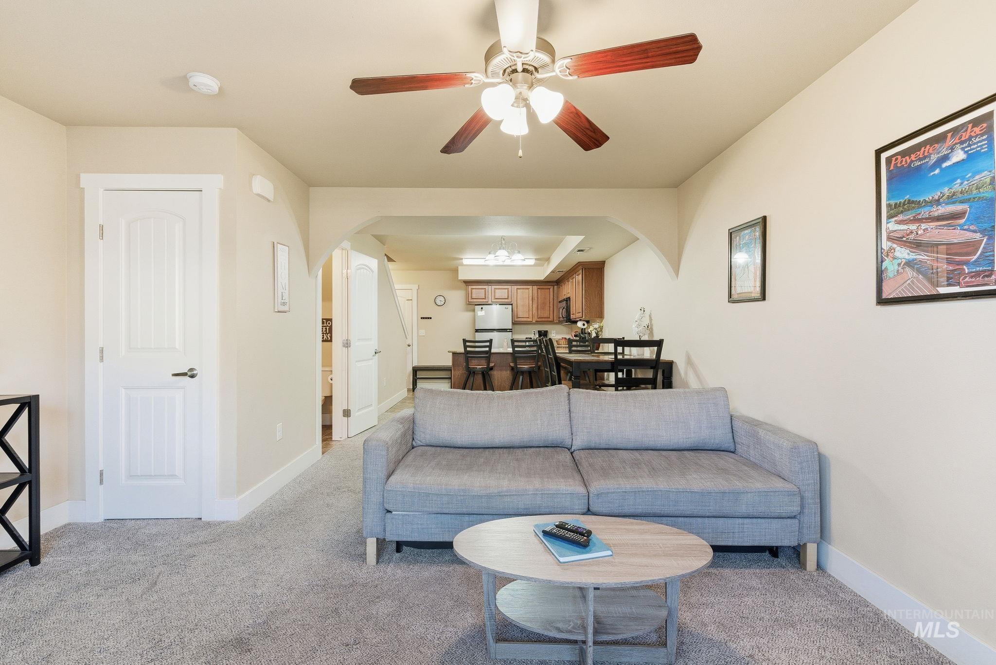 Living area with arched walkways, light carpet, and a ceiling fan
